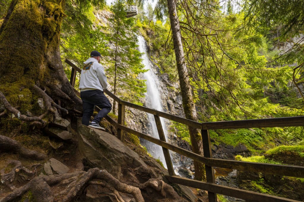Photo of a man in the foreground standing looking at spectacular Plodda falls, near glen affric