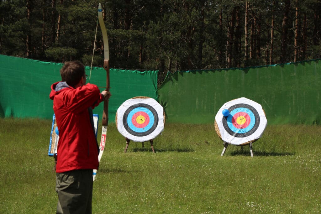 Man about to shoot arrow with bow at archery targets
