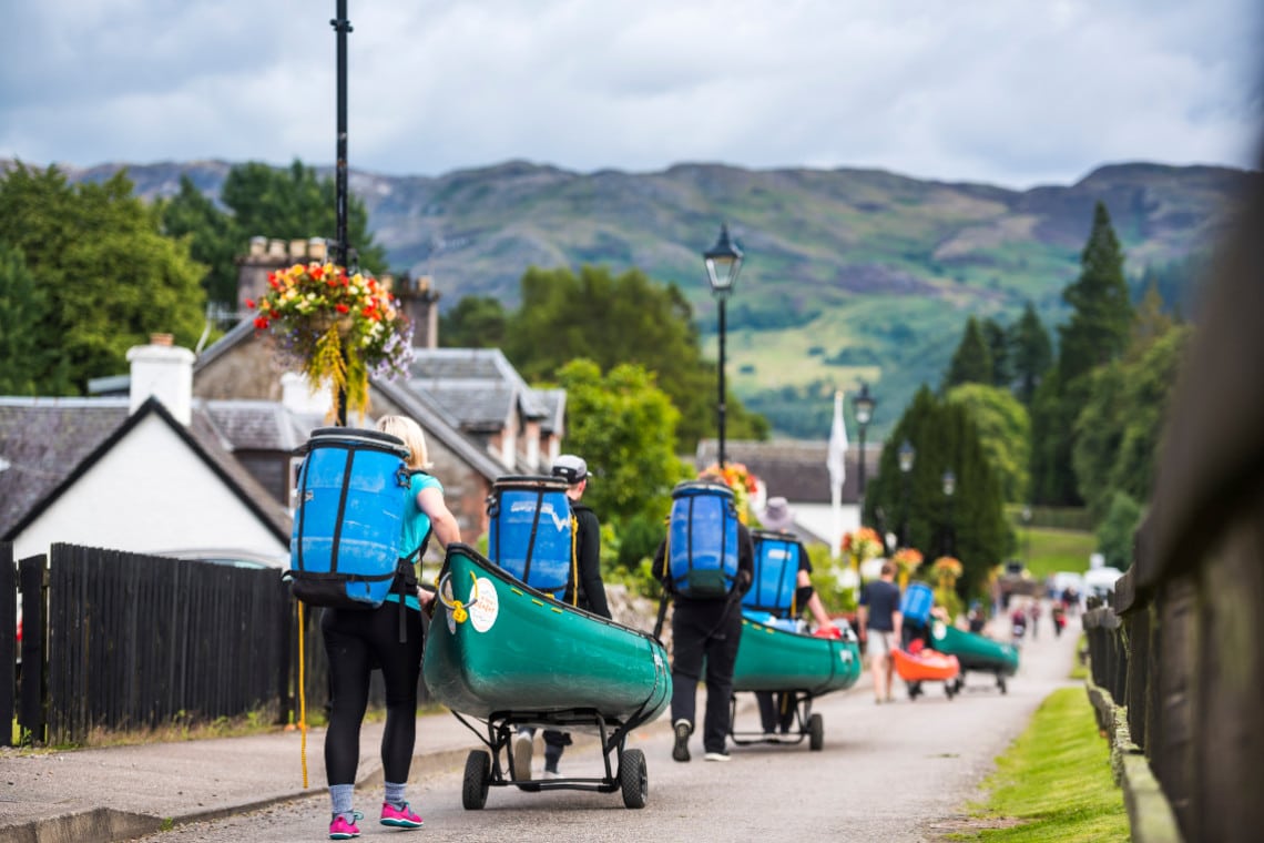 a group of paddlers portaging their canoes and equipment on canoe trollies down a road