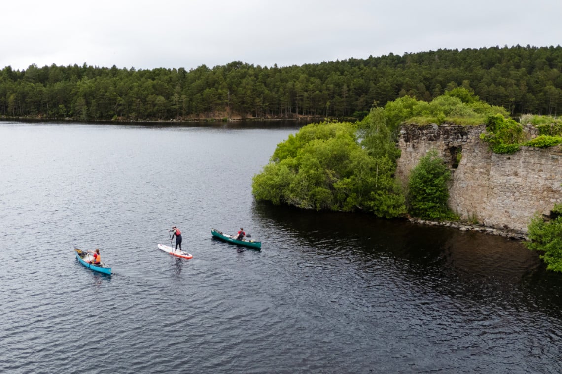 people in canoes and on a paddle board, glide gently past a castle on a highland loch