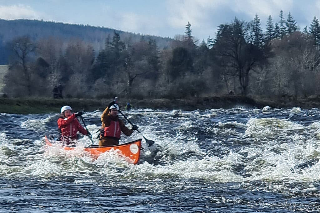 2 people in a canoe riding through rapids on the river spey