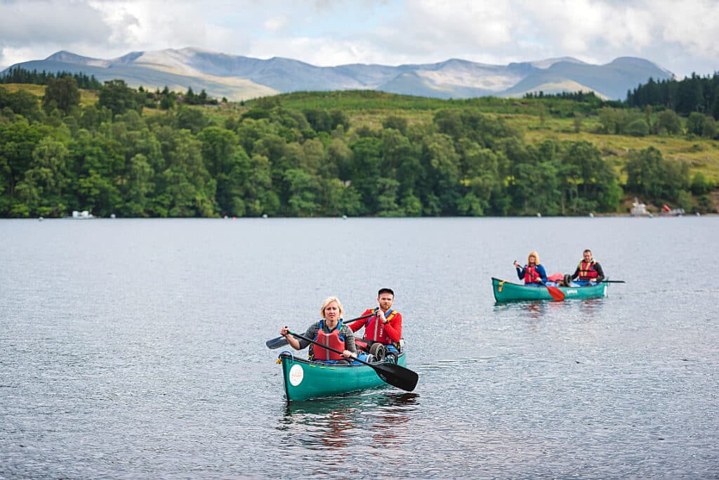 people in 2 canoes, canoeing on a scottish loch with forests and mountains in the background