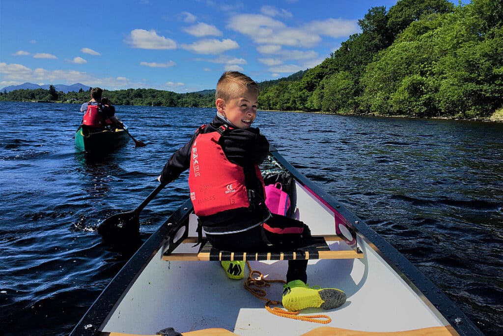 A young boy at front of a canoe on a gentle canoe journey on a scottish loch
