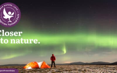 A man standing watching the Northern Lights beside his tent in the Cairngorms Mountain tops