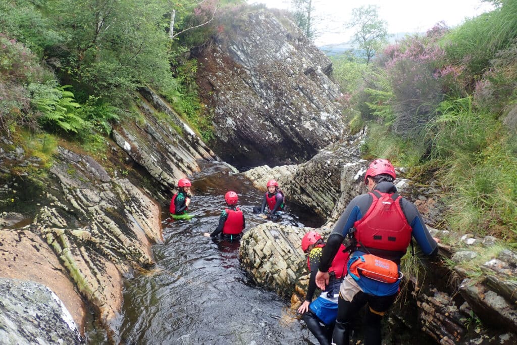 a group in wetsuits and helmets gorge walking in a highland gorge