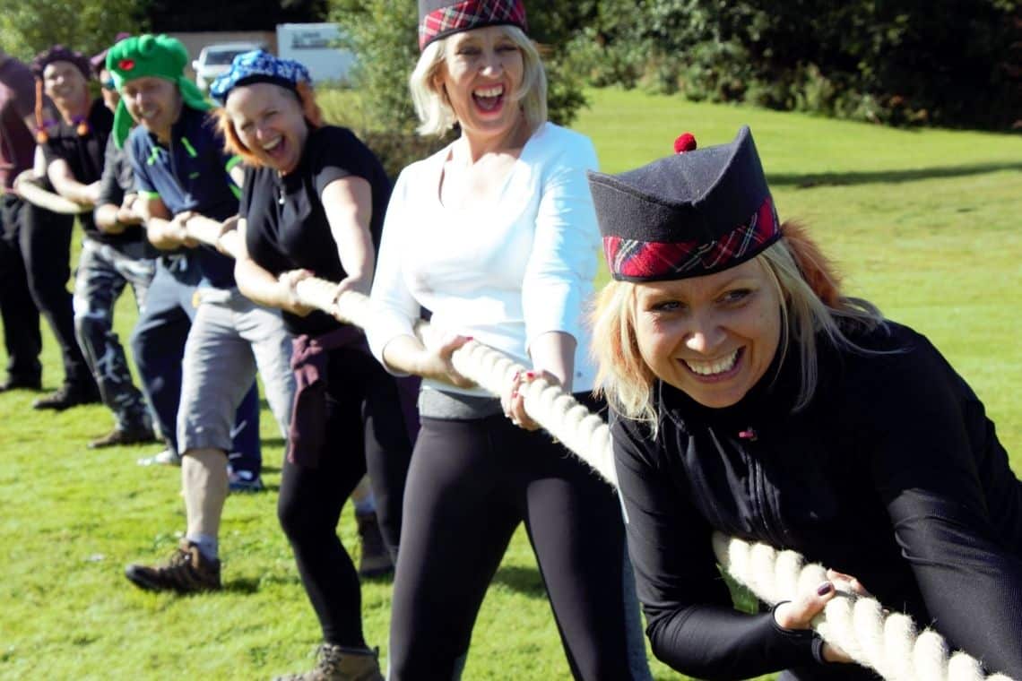 A group of ladies competing in a Highland Games tug of war with big smiles and laughing