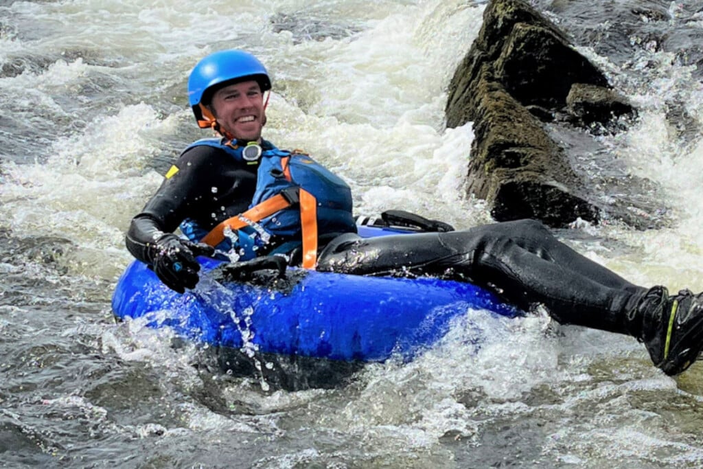 man smiling while river tubing in river rapids