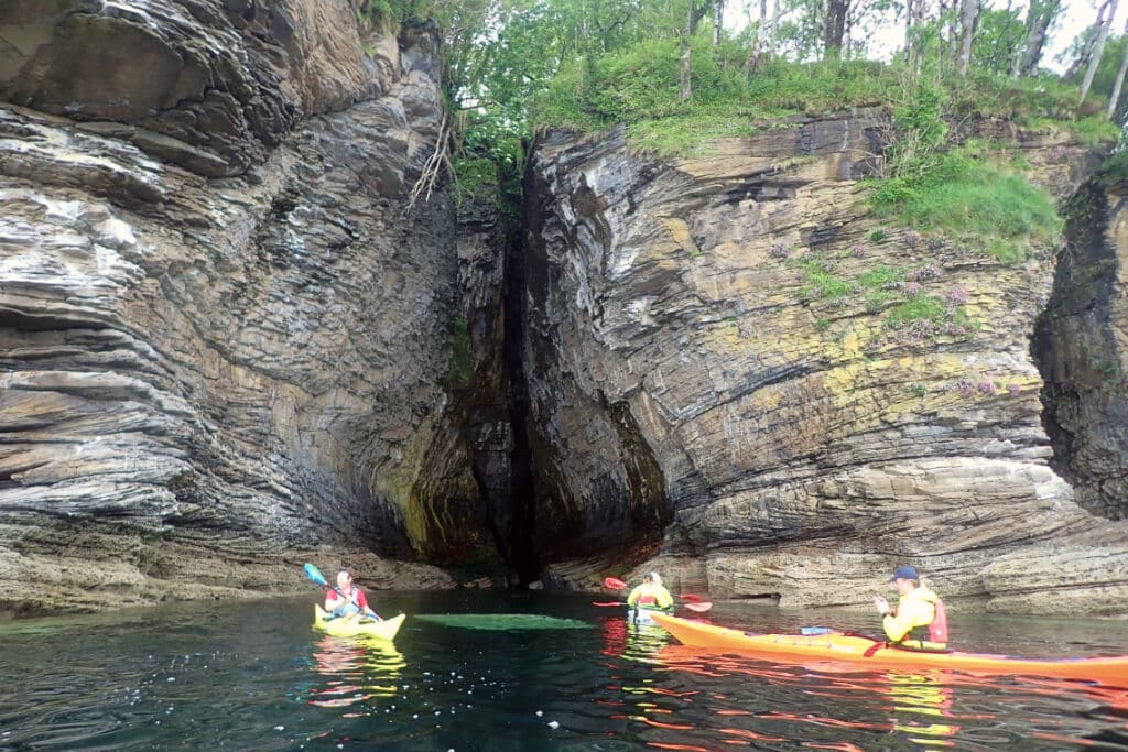 kayaks explore the entrance of a cave in a cliff
