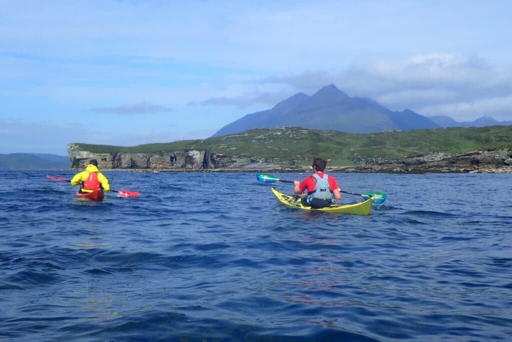 kayakers paddle around the coast of sky, cliffs and mountains as a backdrop