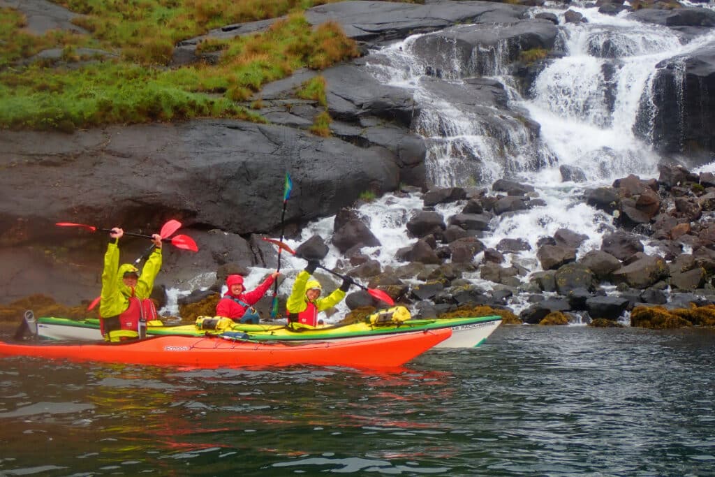 kayakers pose for a phot in front of a water fall in loch scavaig, isle of skye