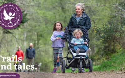 A multi-generational family group of adults and children, one being pushed in a buggy, walking on a woodland trail in the Cairngorms National Park