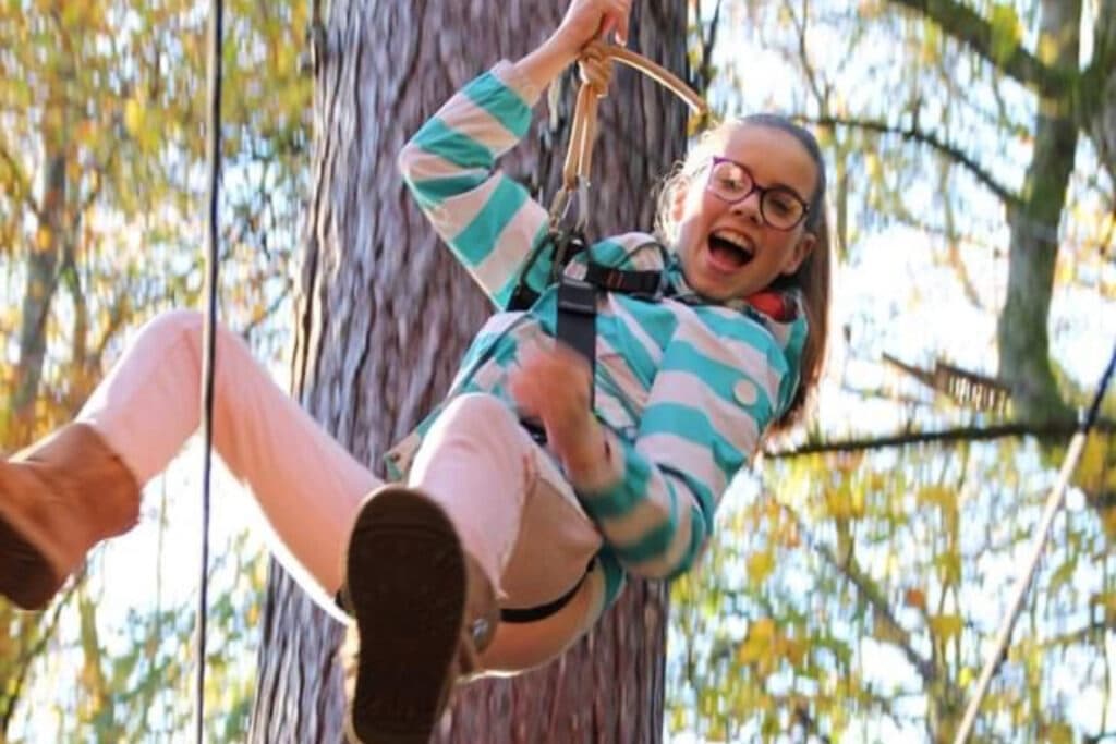 happy smiling girl hanign from zipline rope at treezone
