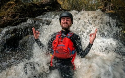 person sitting in a small waterfall while gorge walking with a big smile on their face