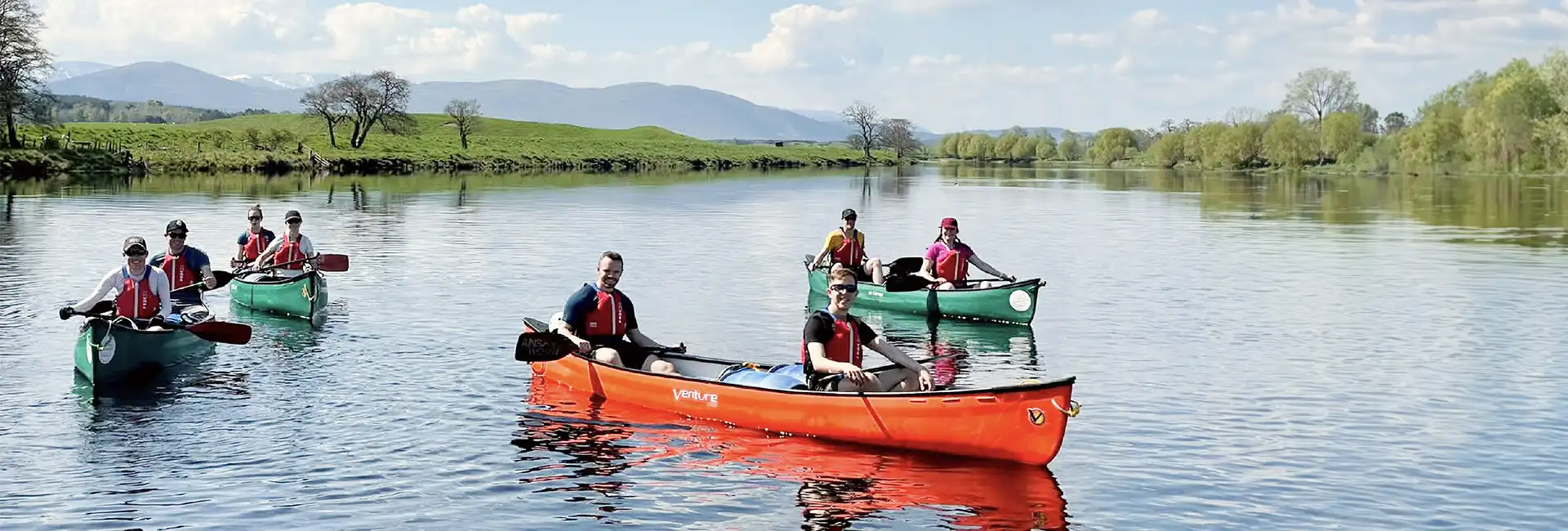Group of smiling people in canoes on sunny day on calm river