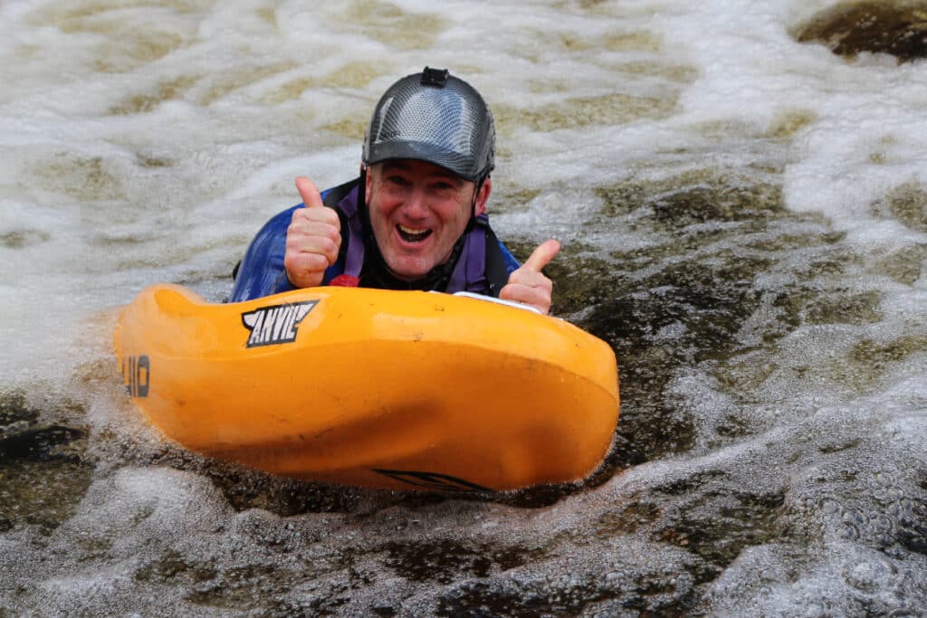 a smiling man with his thumbs up white water river sledging in a highland river