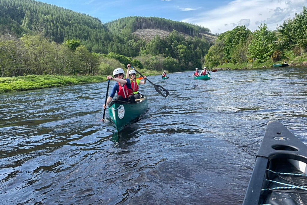2 people canoeing on a gentle stretch of river as part of a canoe expedition