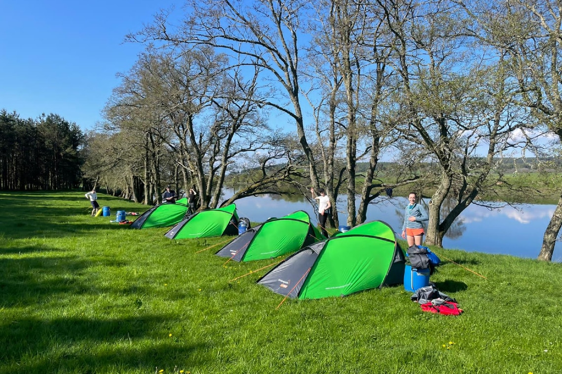 tents lined up on a river bank during a canoe expedition